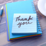 青いボールペンと手帳の上に「Thank you」と書かれたメモ